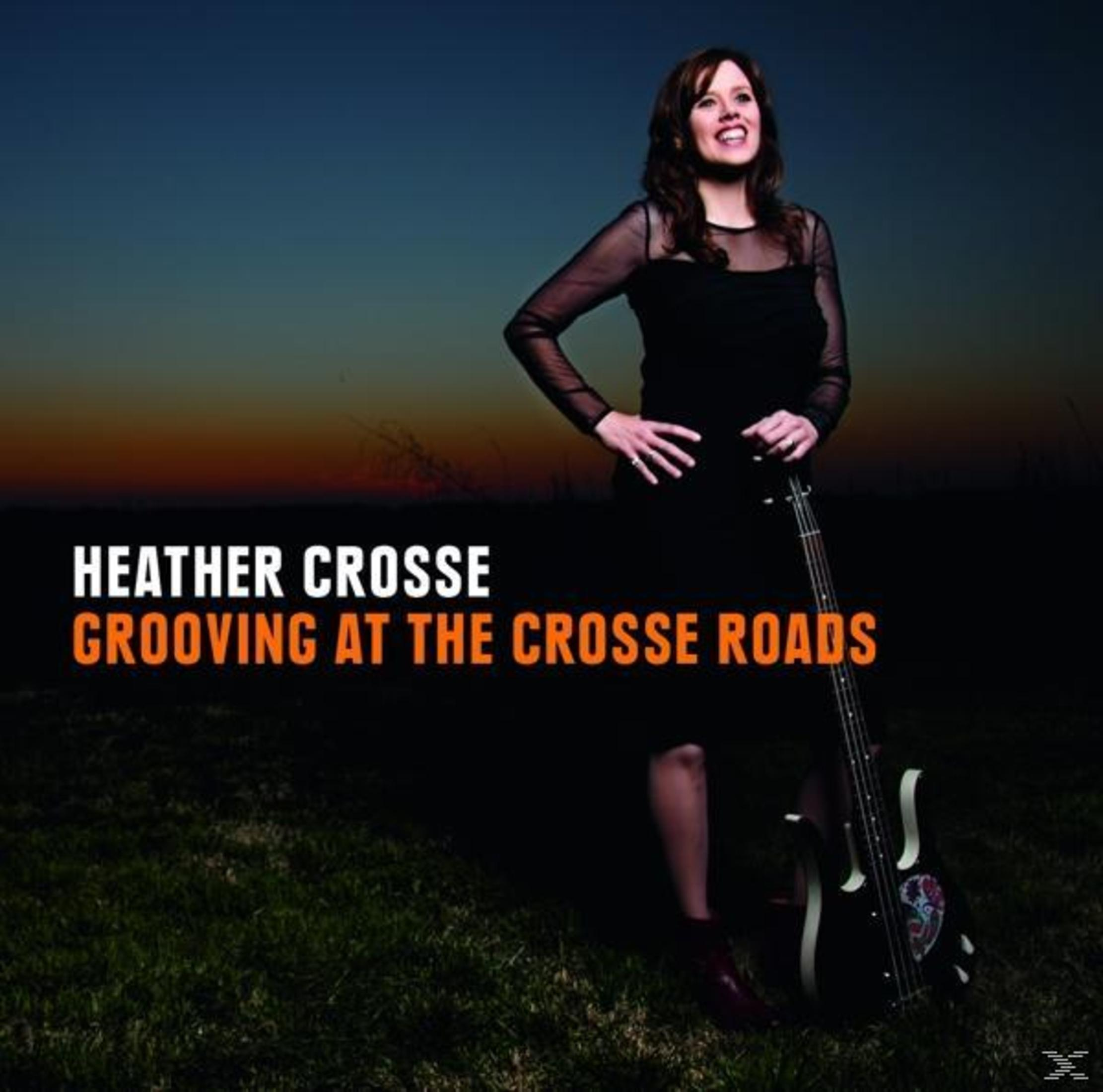 Heather Crosse steht im Freien vor einem dunklen Hintergrund und hält einen E-Bass.
