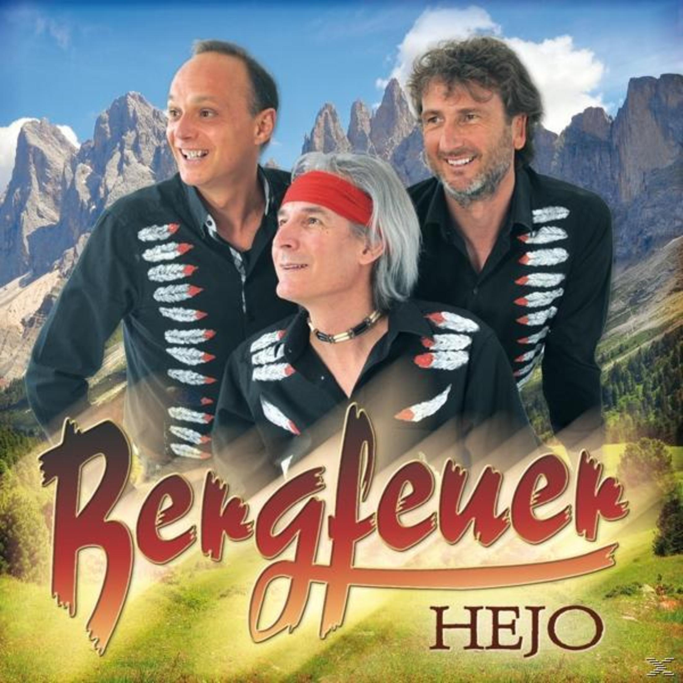 Drei Männer in schwarzen Hemden mit Federmuster vor einer Bergkulisse, unten der Schriftzug Bergfeuer HEJO.