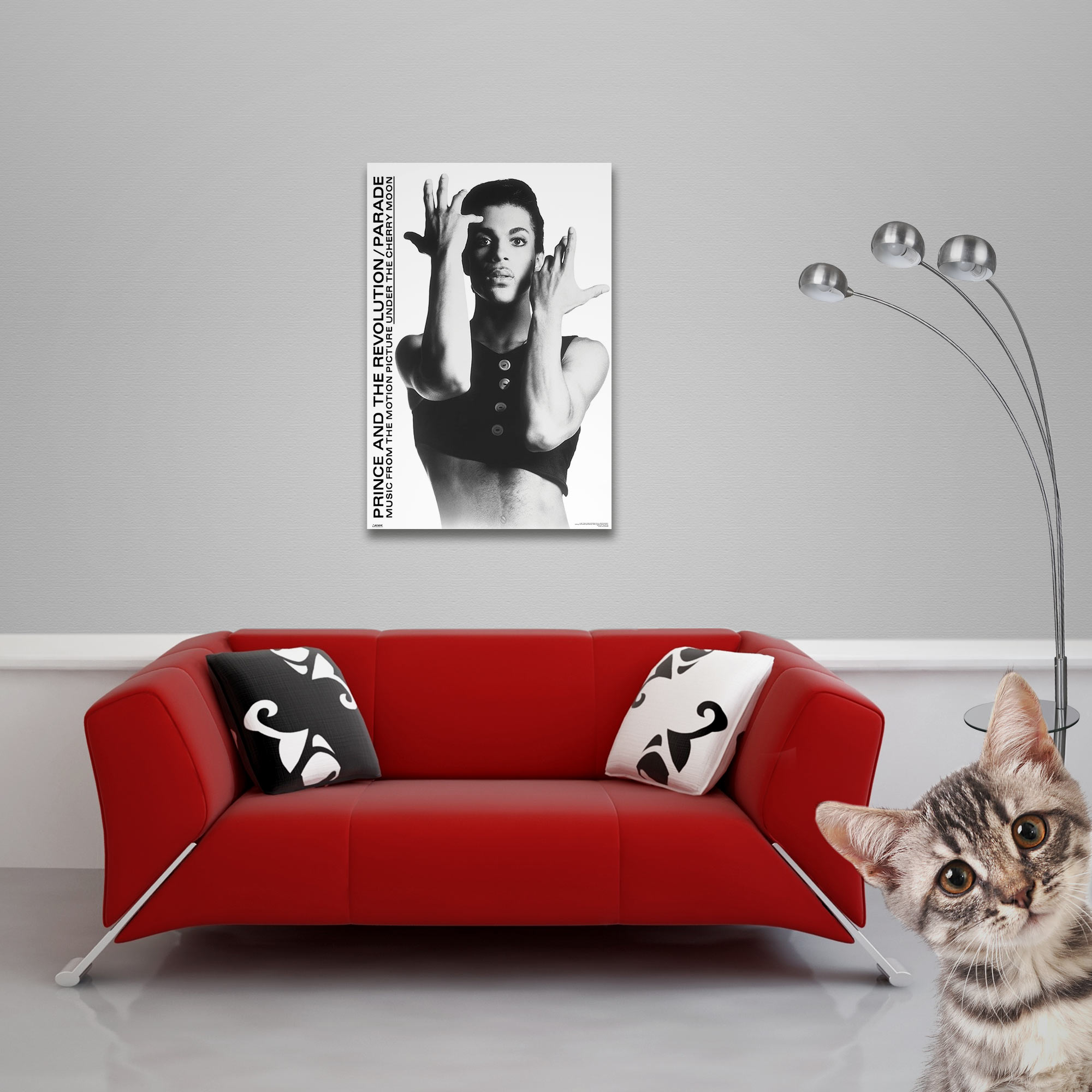 Eine graue Wand zeigt ein Schwarz-Weiß-Poster, darunter ein rotes Sofa mit Kissen und eine Katze.