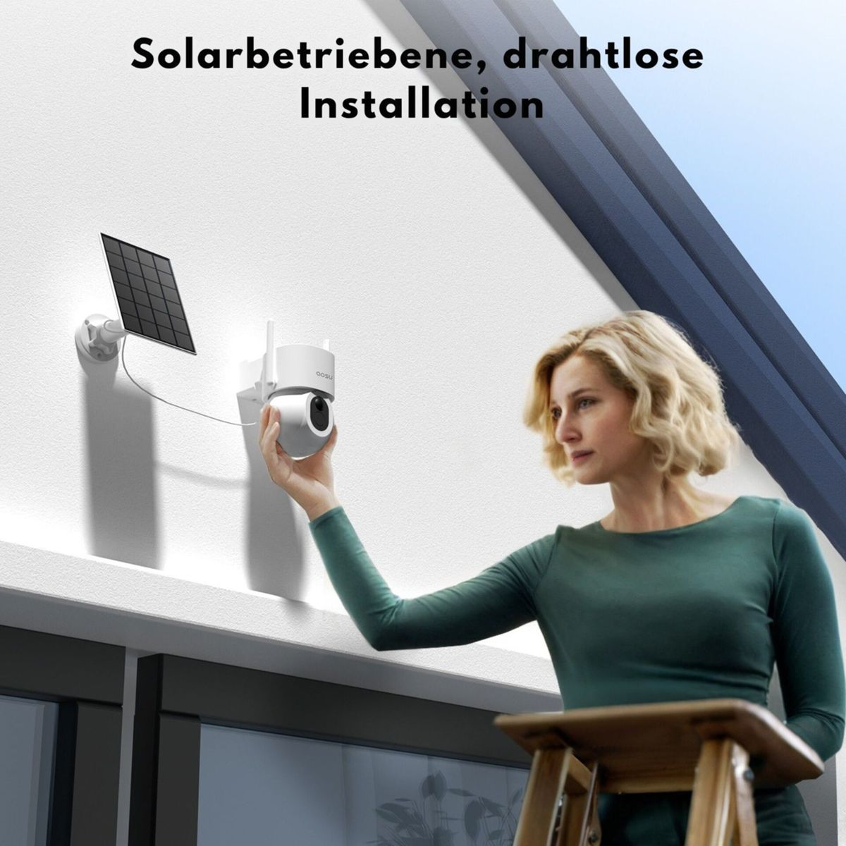 Eine Frau in grünem Oberteil montiert eine weiße Überwachungskamera mit Solarpanel an der Außenwand.
