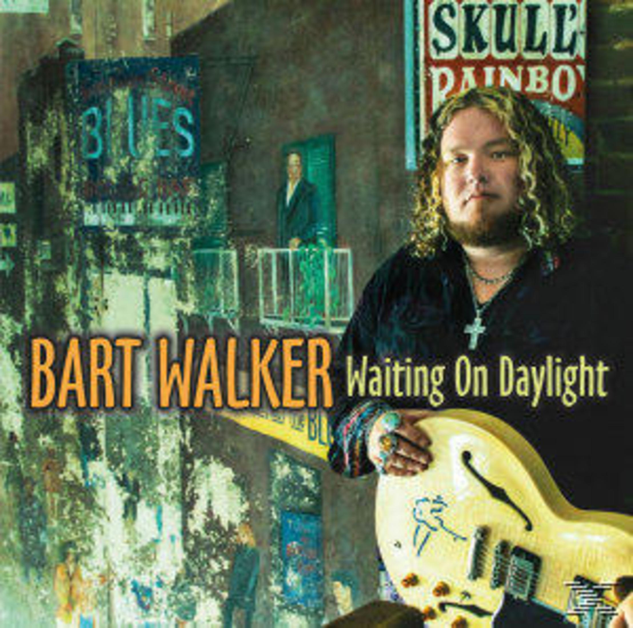 Musiker Bart Walker hält eine Gitarre vor einer bemalten städtischen Wand.