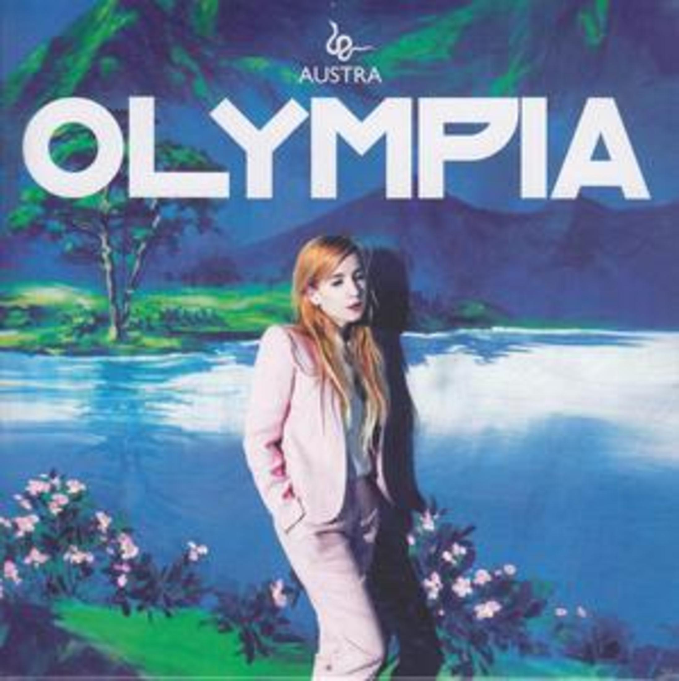 Eine blonde Frau im rosa Hosenanzug steht vor einer gemalten Landschaft mit Fluss und Text 'OLYMPIA'.