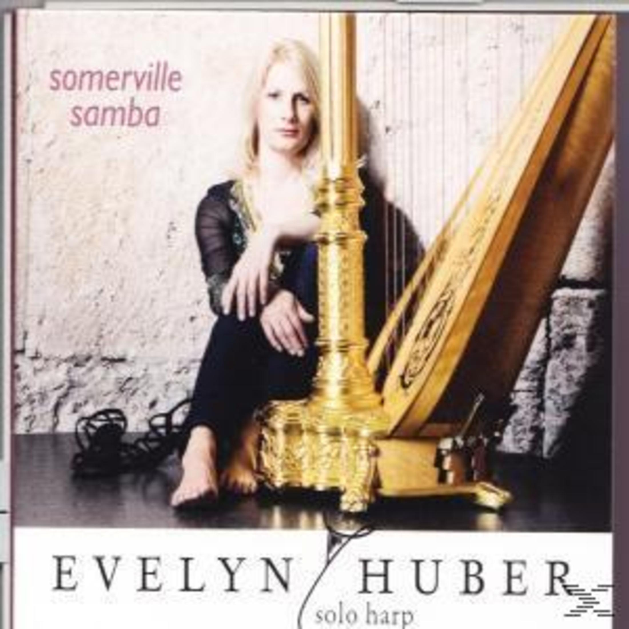 Evelyn Huber sitzt barfuß neben einer goldenen Harfe vor einer steinernen Wand, Text zeigt Somerville Samba.