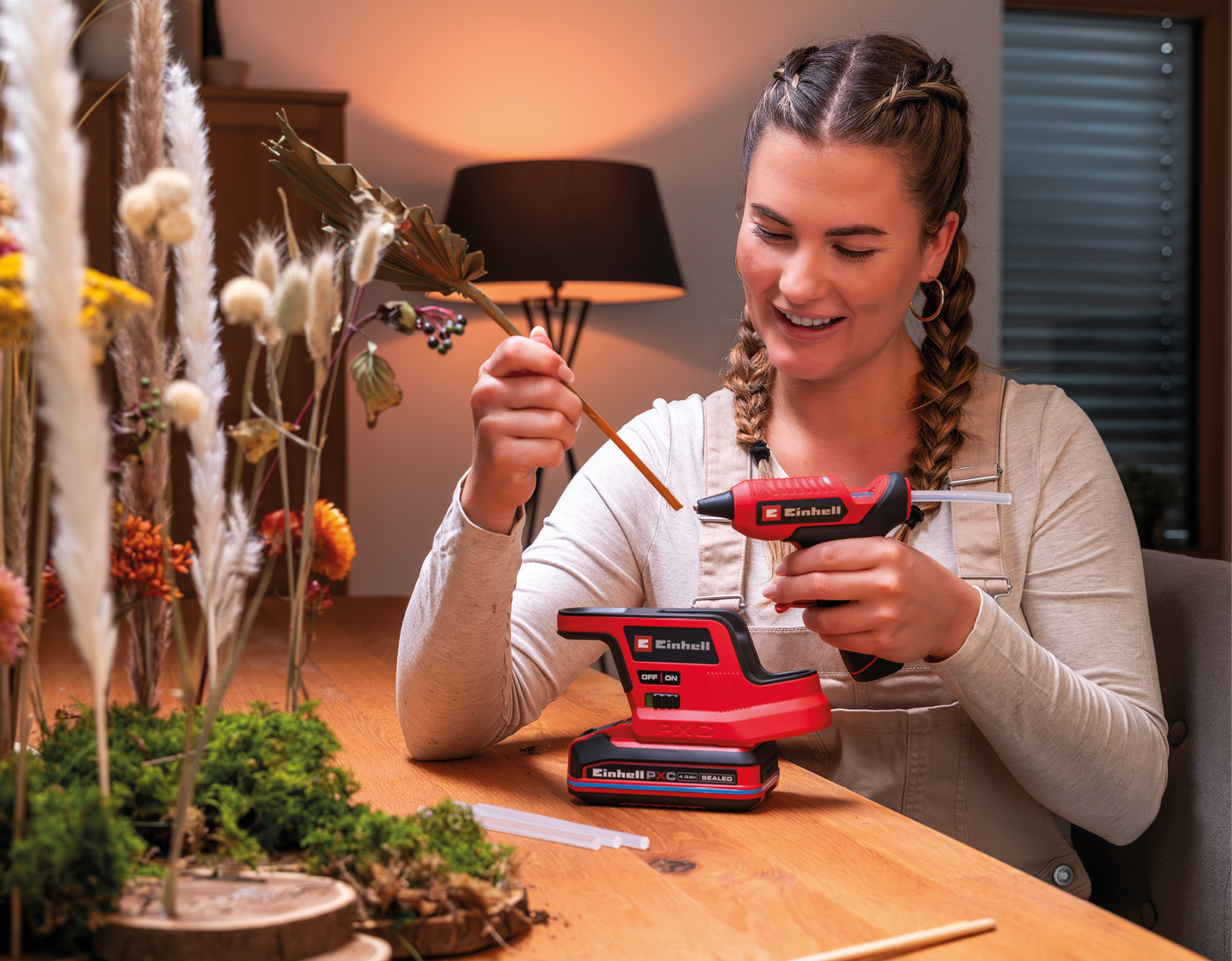 Eine Frau craftet mit einer roten Einhell Heißklebepistole und Akkustation am Holztisch.