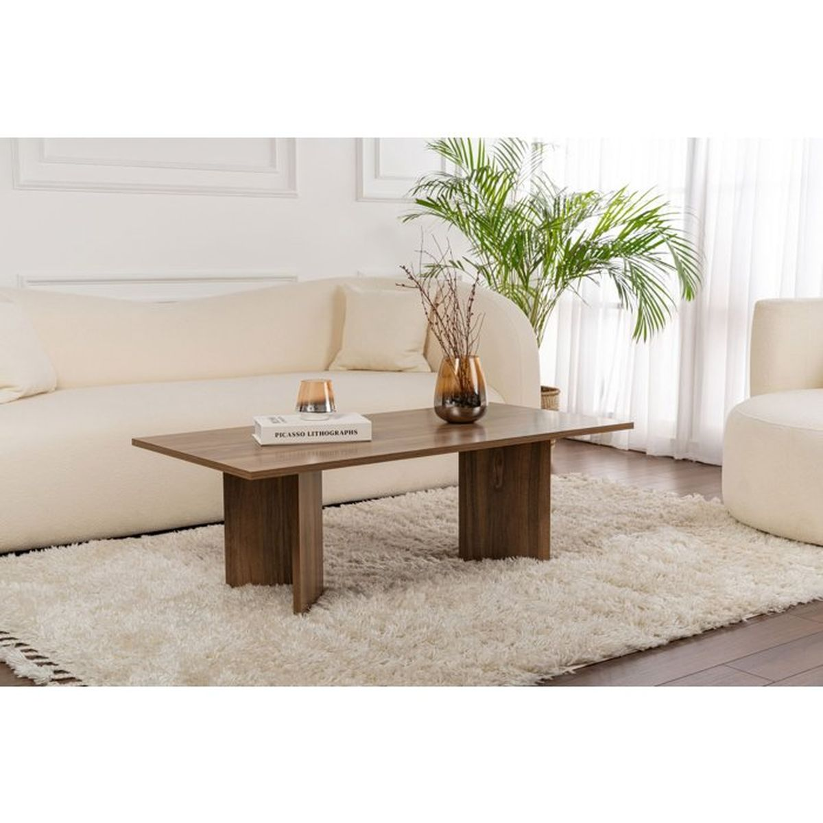 Ein hölzerner Couchtisch auf einem hellen Teppich vor einem weißen Sofa mit dekorativer Vase und Buch.