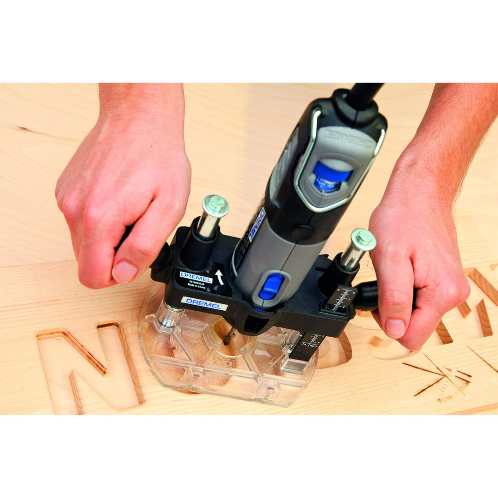 Hände halten eine Dremel-Fräse auf einer Holzoberfläche mit ausgeschnittenen Buchstaben.