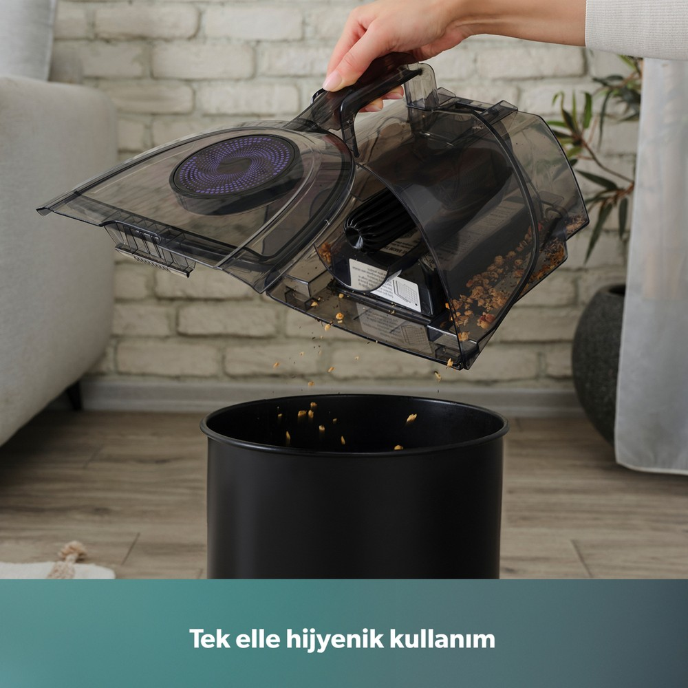 Bir el, tuğla duvar önündeki siyah çöpe şeffaf elektrikli süpürge haznesini boşaltıyor.