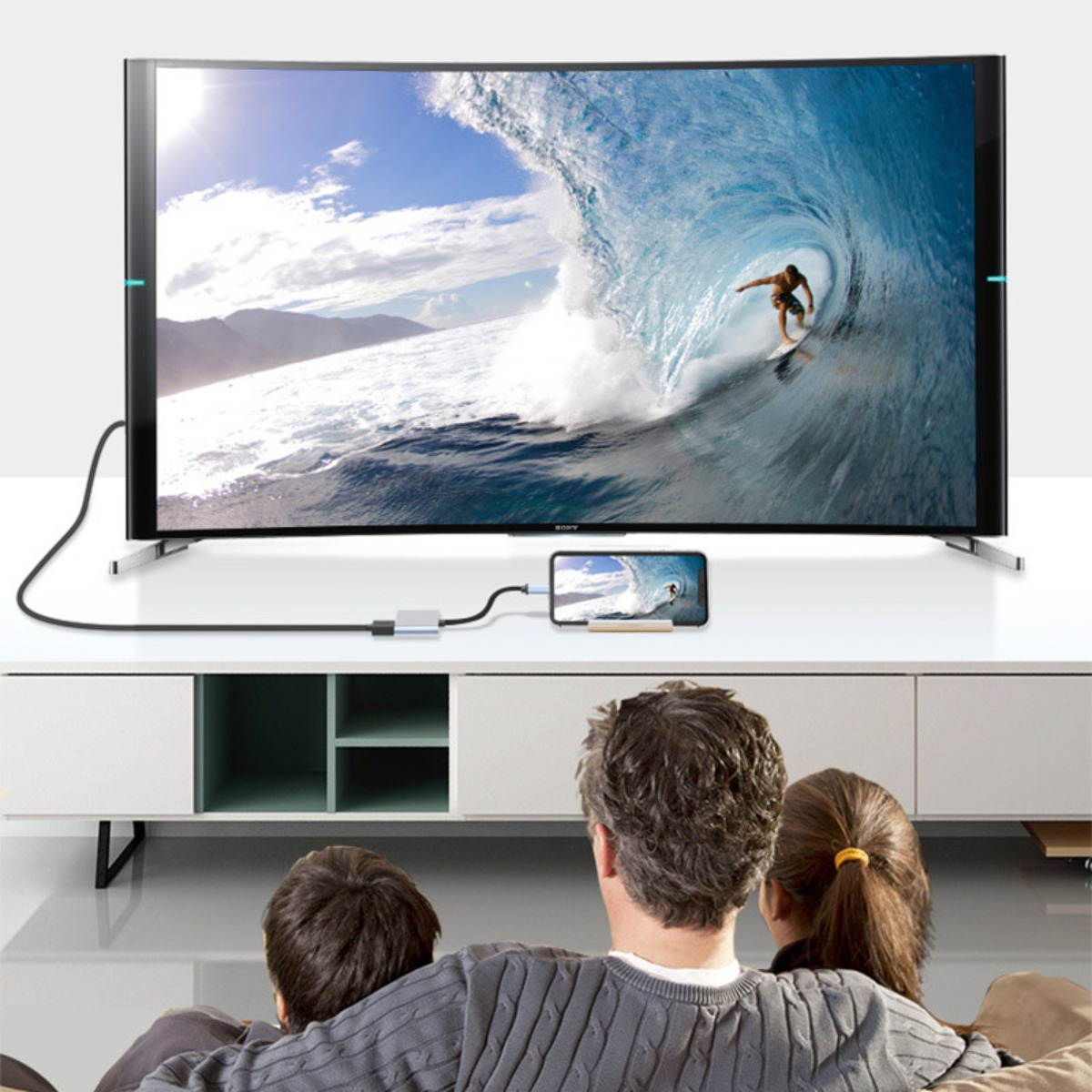 Rodzina ogląda telewizor wyświetlający zawartość smartfona połączonego kablem.