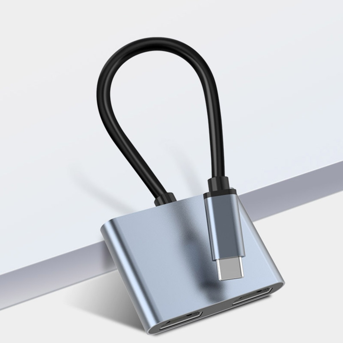 Szary hub USB-C z krótkim czarnym kablem i srebrnym złączem na białej powierzchni.