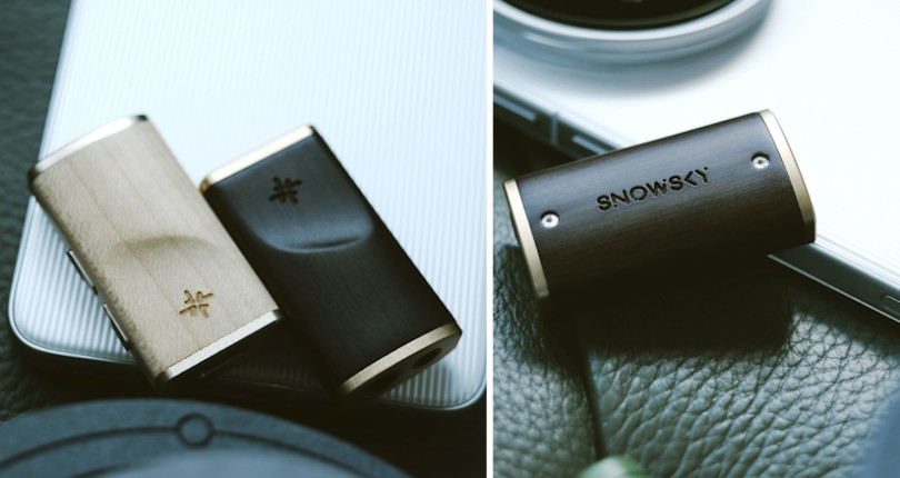 Dwa małe drewniane i metalowe urządzenia Snowsky DAC leżą na błyszczącej powierzchni obok smartfona.