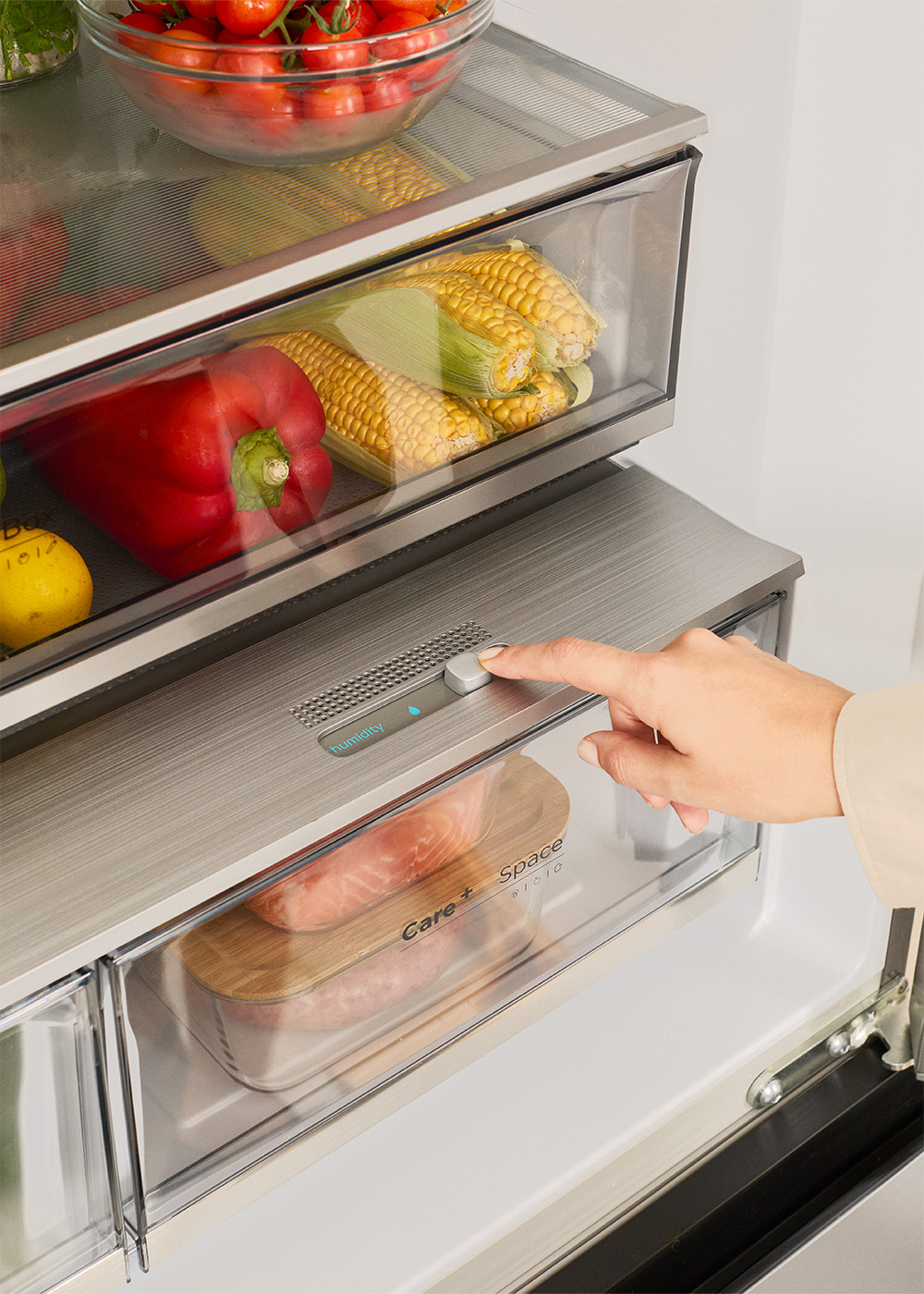 Una mano ajusta el control de humedad en el cajón de la nevera lleno de verduras frescas y carne.