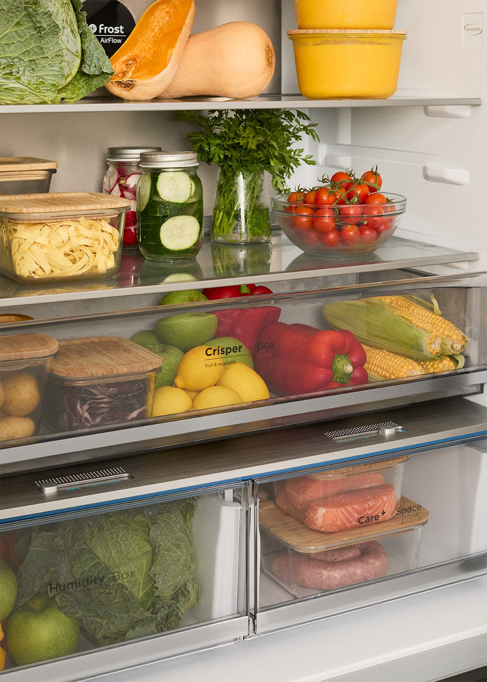 Una nevera bien surtida con verduras frescas, frutas, hierbas, pepinillos, pasta y carne en los compartimentos.