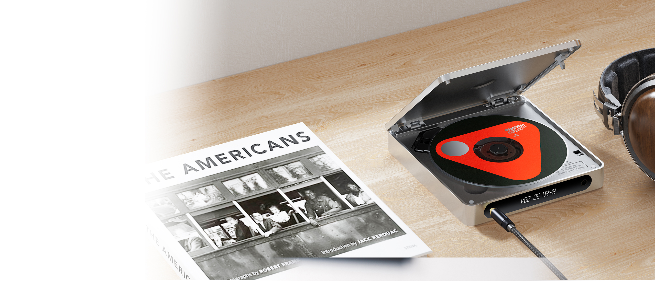 Srebrny odtwarzacza CD odtwarza płytę, obok książki zatytułowanej The Americans na drewnianym stole.