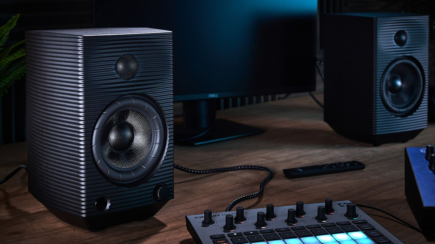 Dwa czarne monitory studyjne i mikser audio z niebieskimi przyciskami stoją na drewnianym biurku.