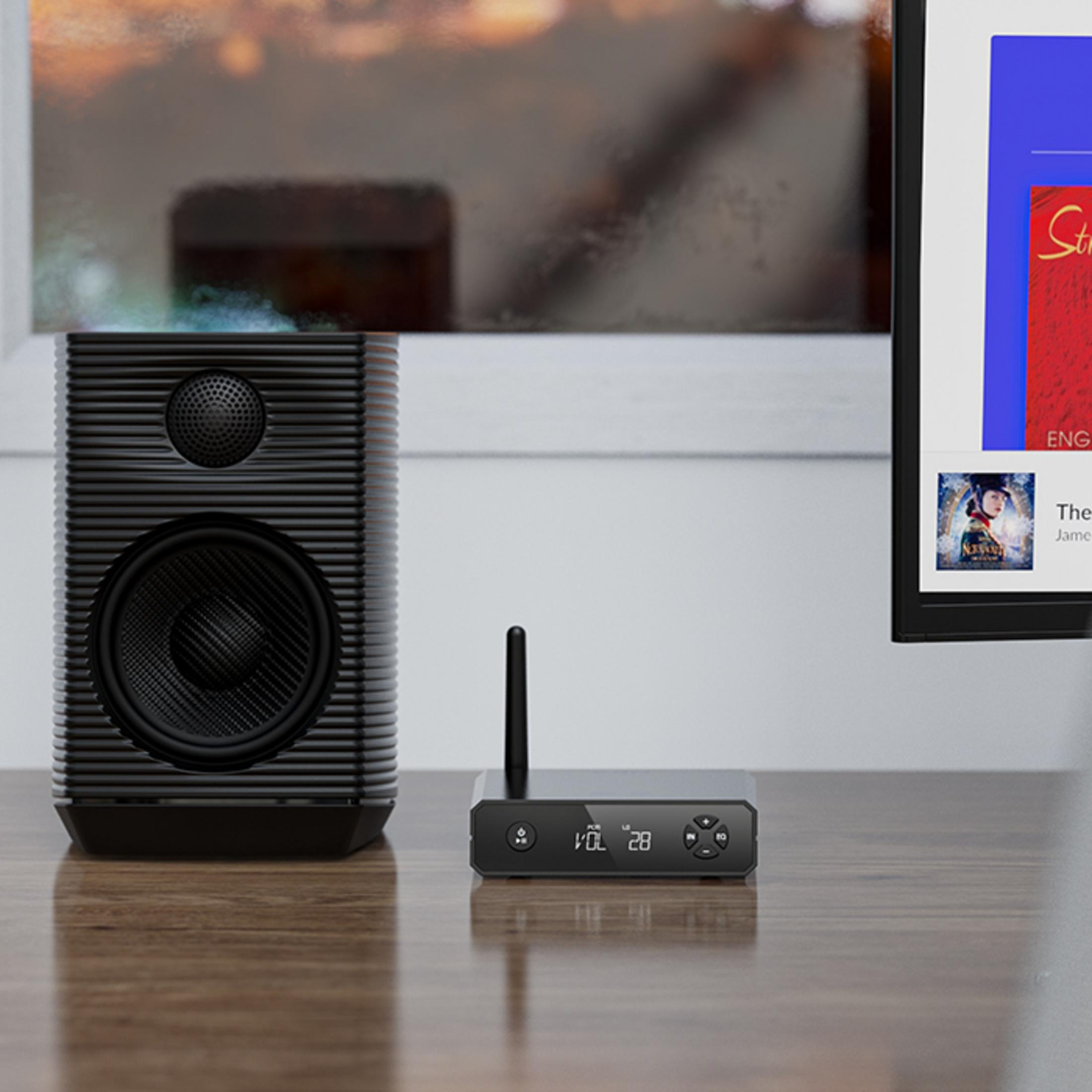 Czarny głośnik i mała skrzynka audio z anteną stoją na drewnianym stole przed oknem.