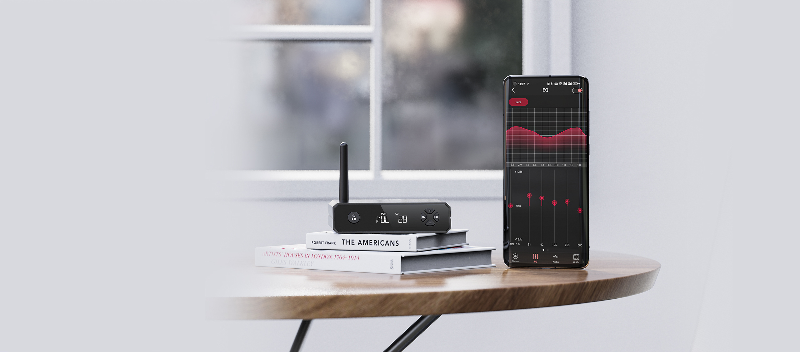 Wzmacniacz audio na książkach i smartfon z aplikacją equalizera na drewnianym stole.