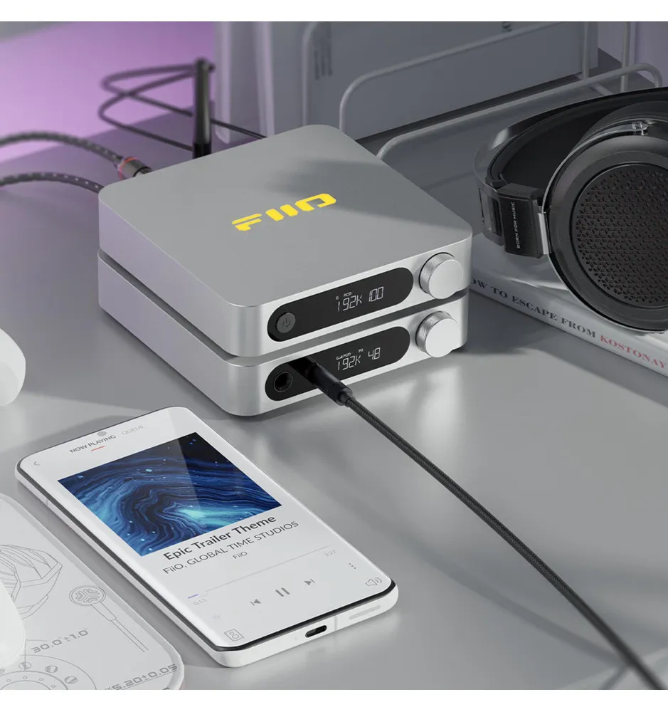 Stylowy zestaw audio ze stosem wzmacniaczy FiiO, podłączonym smartfonem i słuchawkami na szarym biurku.