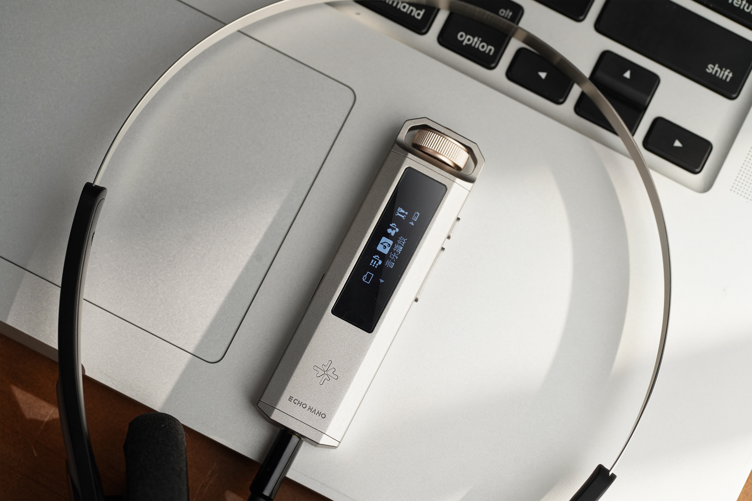 Urządzenie audio Echo Nano z ekranem i pokrętłem głośności leżące na laptopie obok słuchawek.