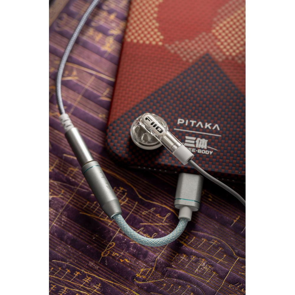 Auricolari trasparenti FiiO con cavo argentato su sfondo fantasia.