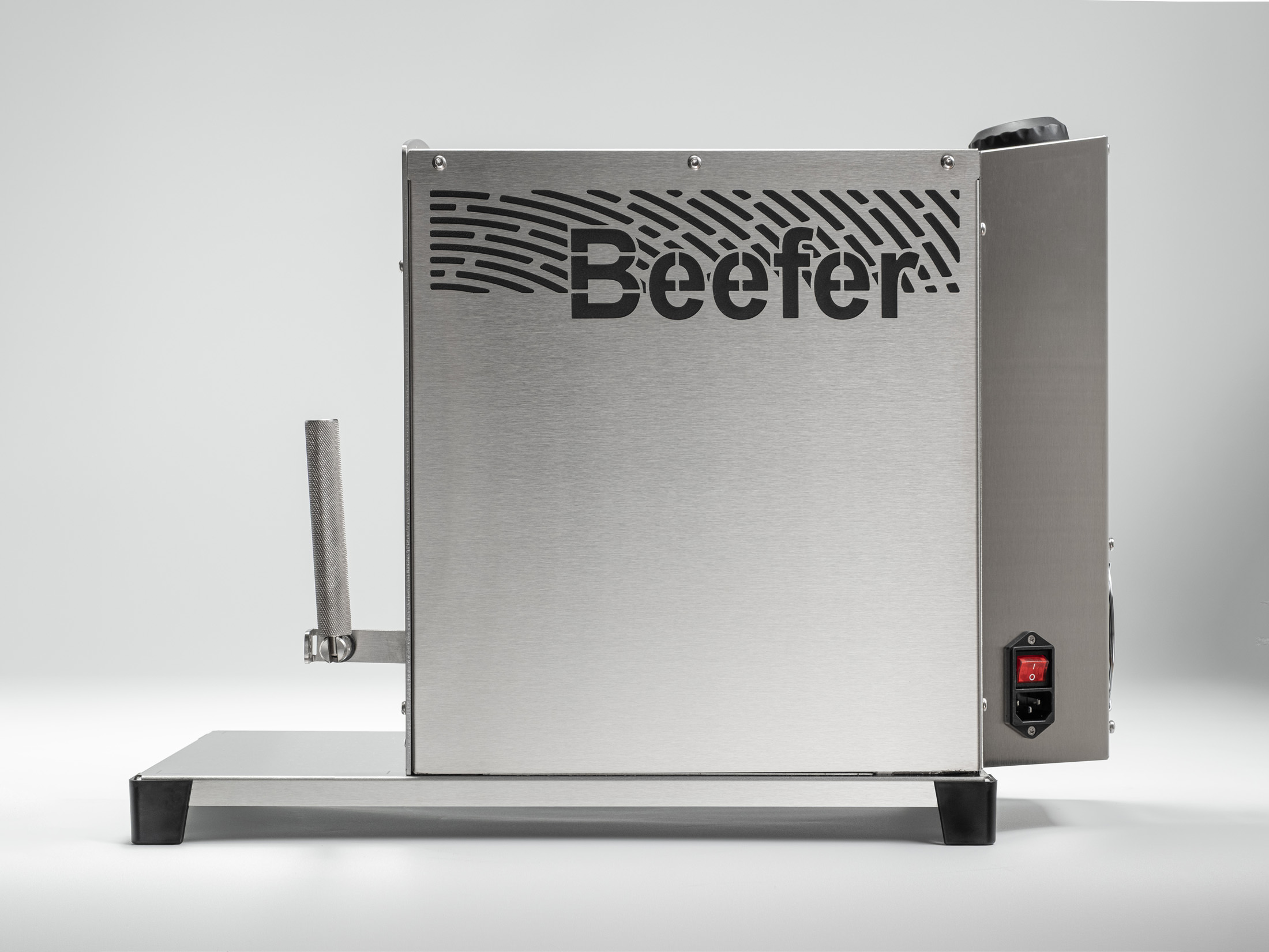Seitenansicht eines silbernen Beefer-Grills mit Edelstahlgehäuse, Griff und rotem Schalter auf hellem Hintergrund.