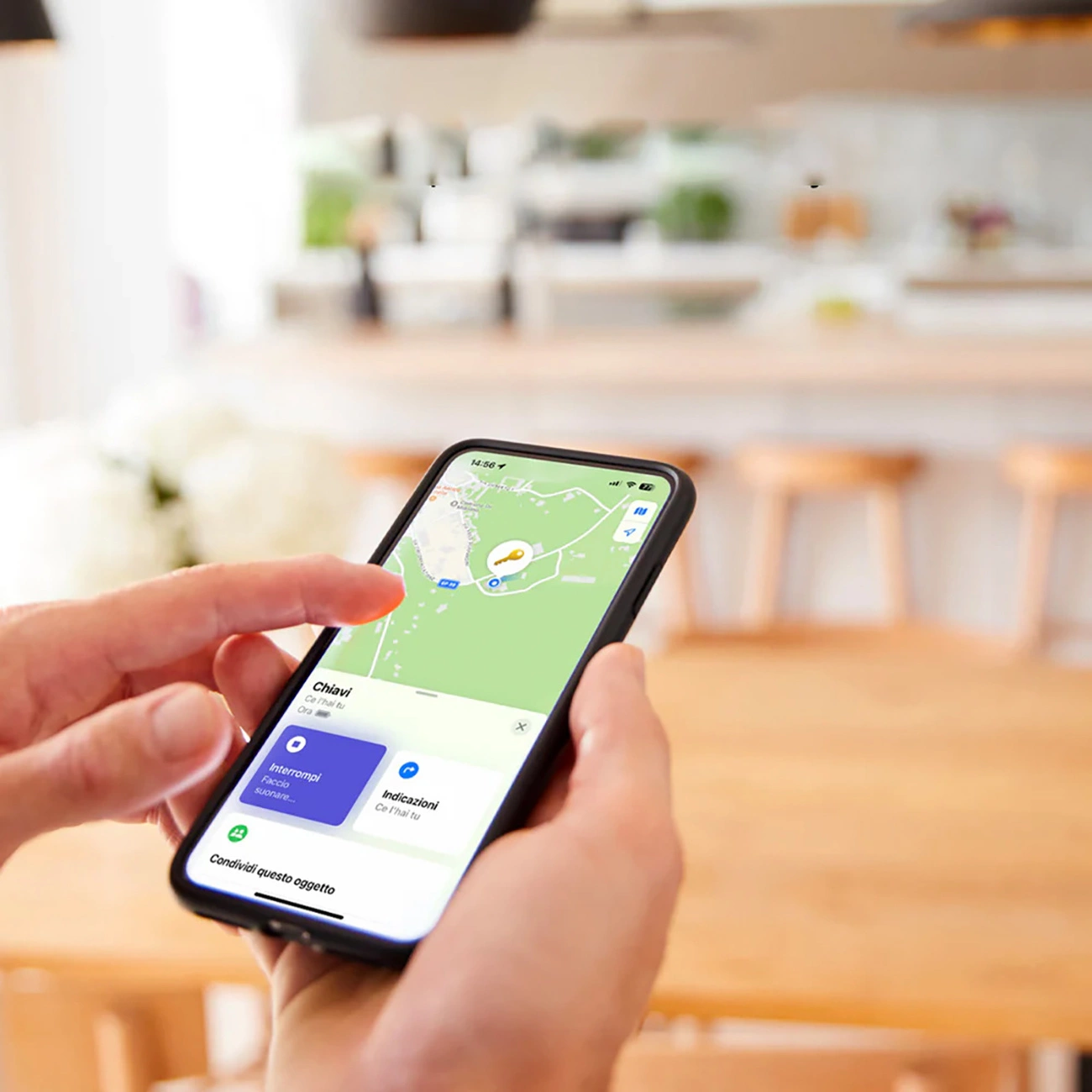 Una persona sostiene un smartphone con una app de mapas y un icono de llave en una cocina luminosa.