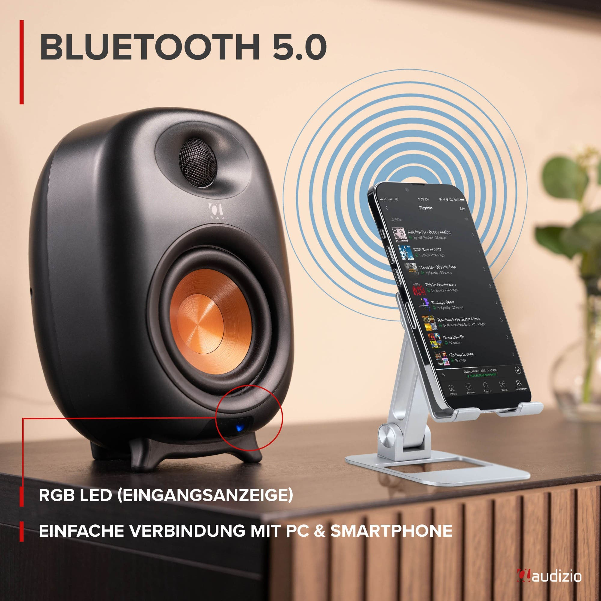 Ein schwarzer Bluetooth-Lautsprecher neben einem Smartphone auf einem Ständer, das Signalwellen aussendet.