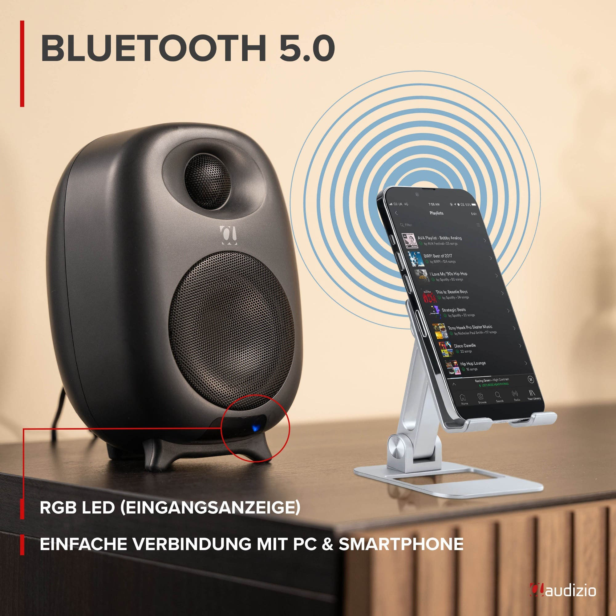 Ein schwarzer Lautsprecher steht neben einem Smartphone auf einem Ständer mit blauen Bluetooth-Wellen.