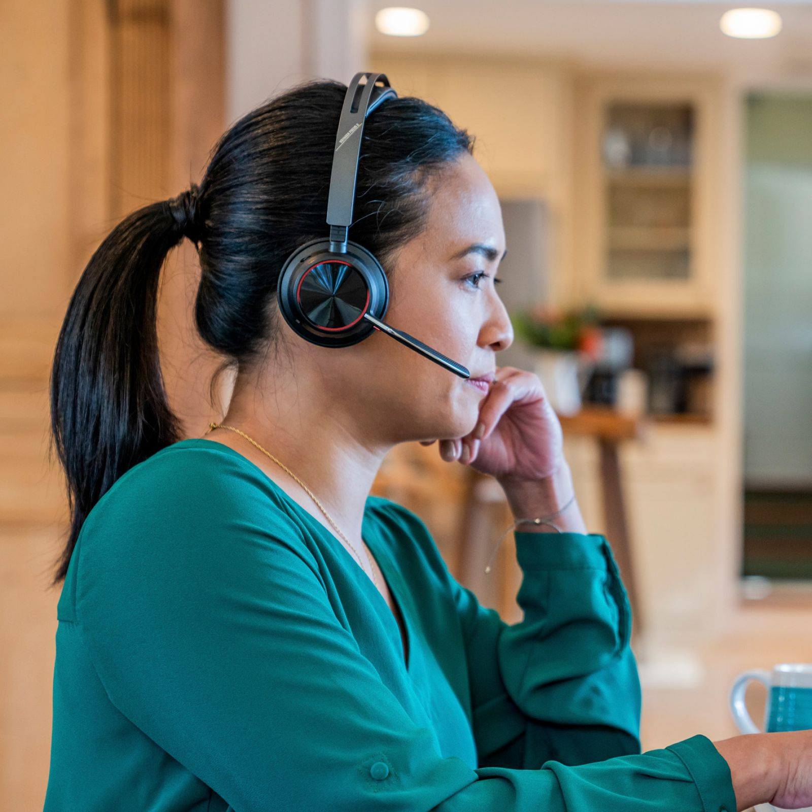 Mujer con coleta y blusa verde usando auriculares en una cocina.