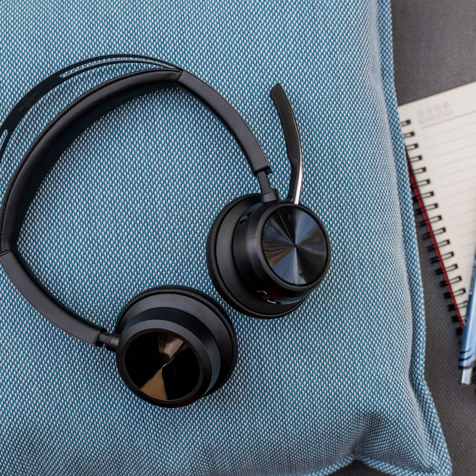 Auriculares negros con micrófono en un cojín azul junto a un cuaderno.