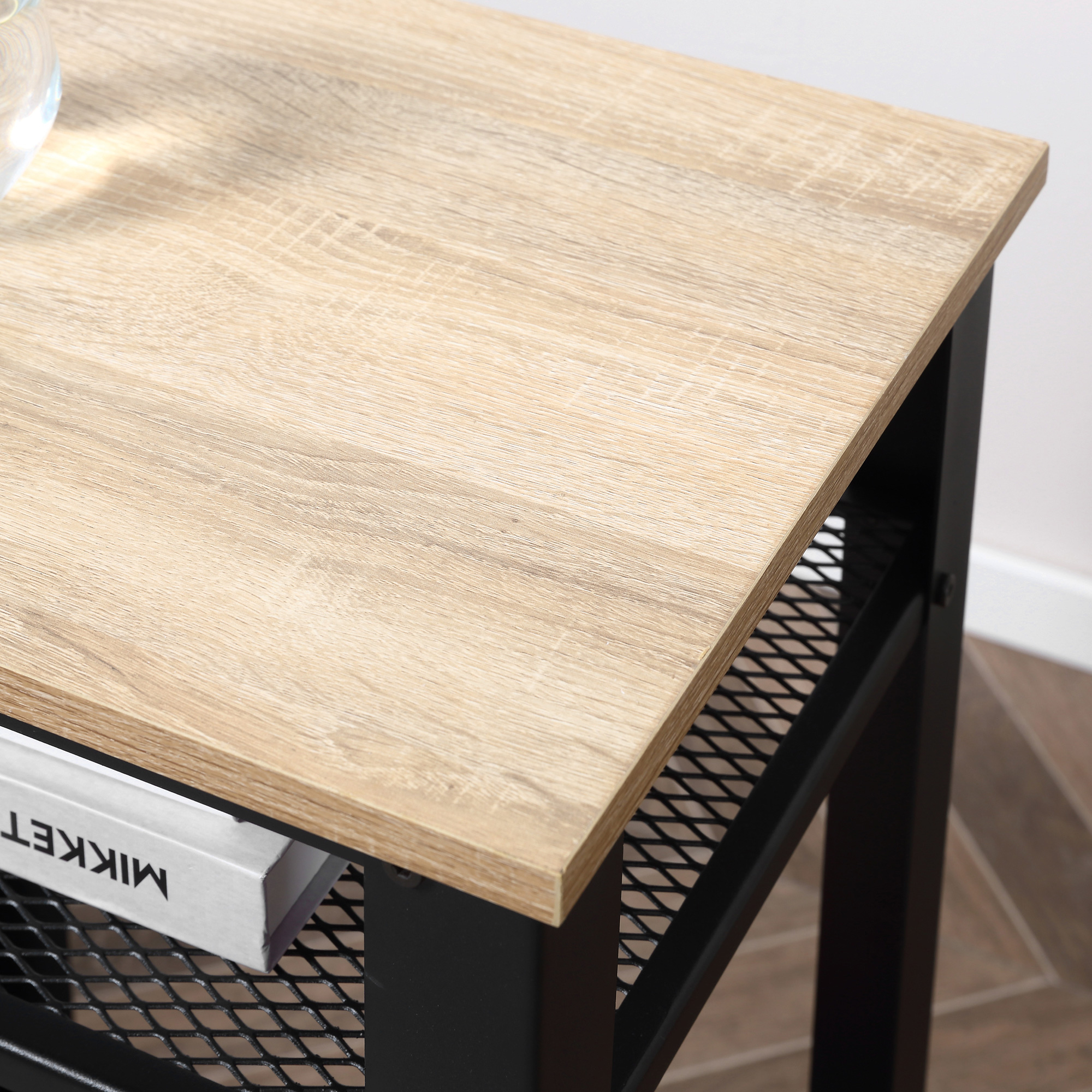 Mesa auxiliar con tablero de madera clara, estructura de metal negro y estante de malla inferior con un libro.