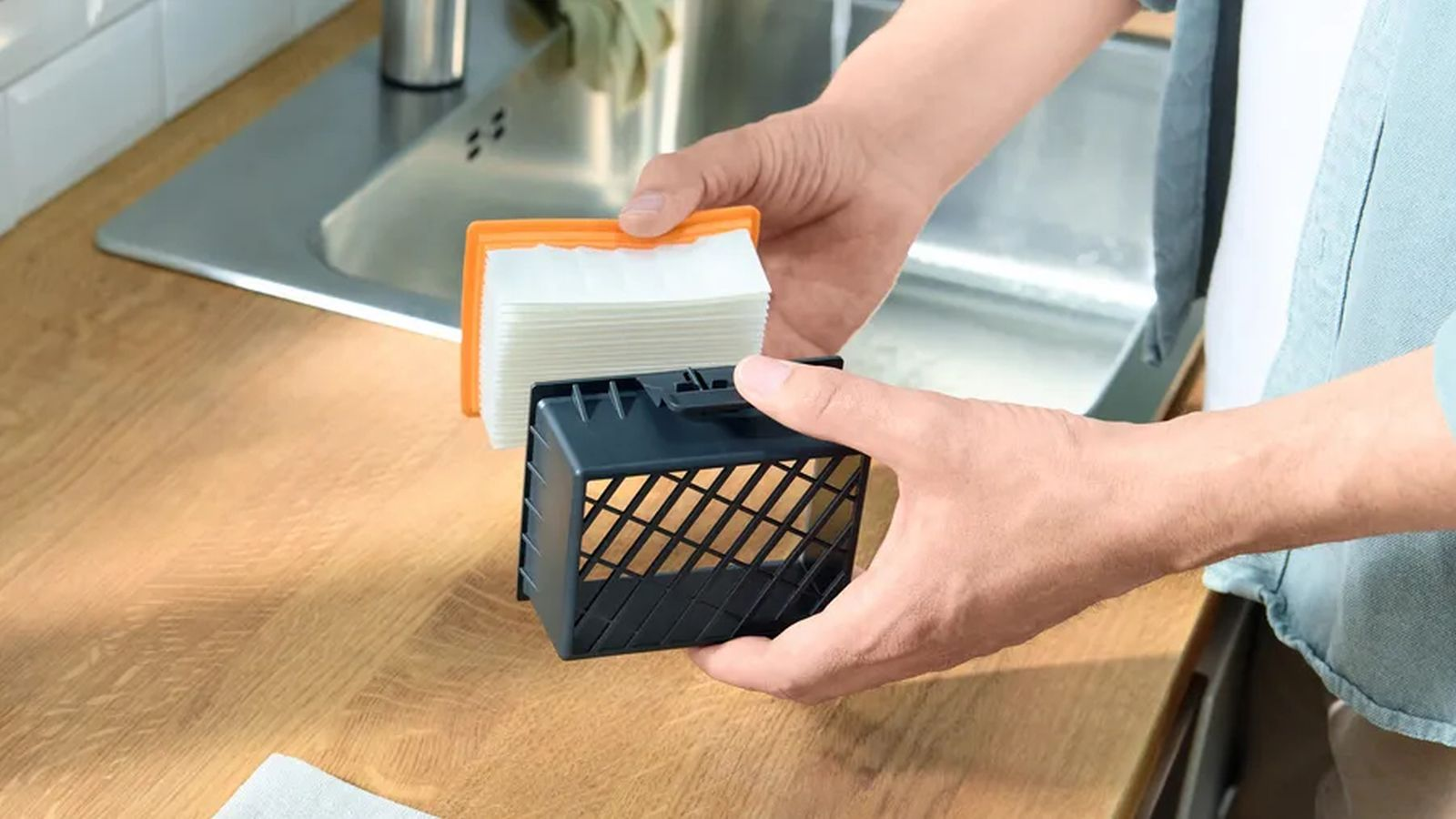 Una persona sosteniendo un filtro blanco sobre un recipiente de malla negra en una cocina.