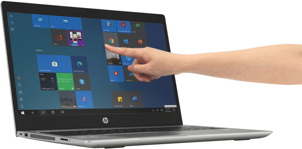 Una mano toca la pantalla táctil de un portátil plateado con el menú de inicio de Windows.