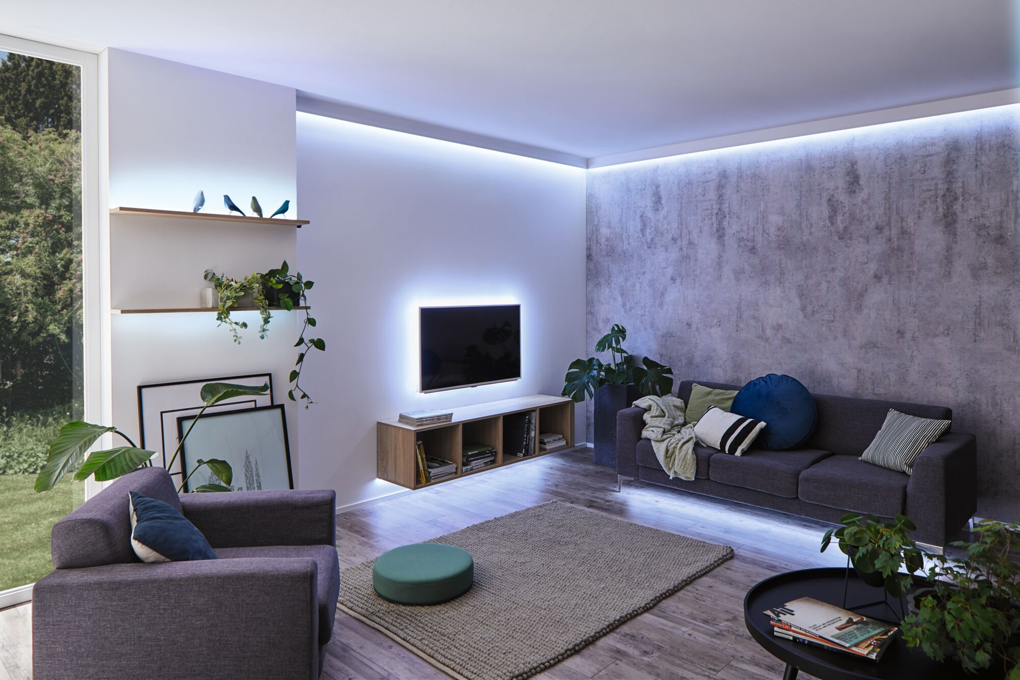 Wohnzimmer mit Sofa, Sesseln, wandmontiertem TV, Holzeinheiten und blauer LED-Hintergrundbeleuchtung.