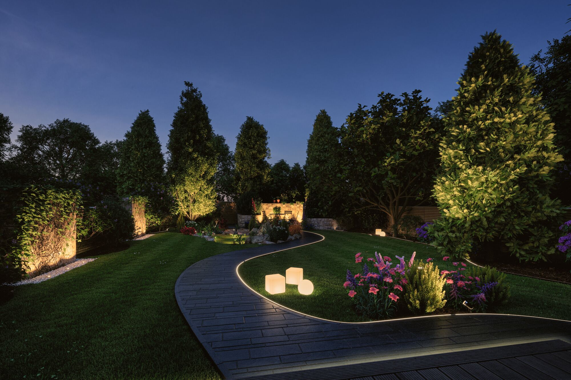 Beleuchteter Garten bei Nacht mit gepflastertem Weg, Blumen und Bäumen.