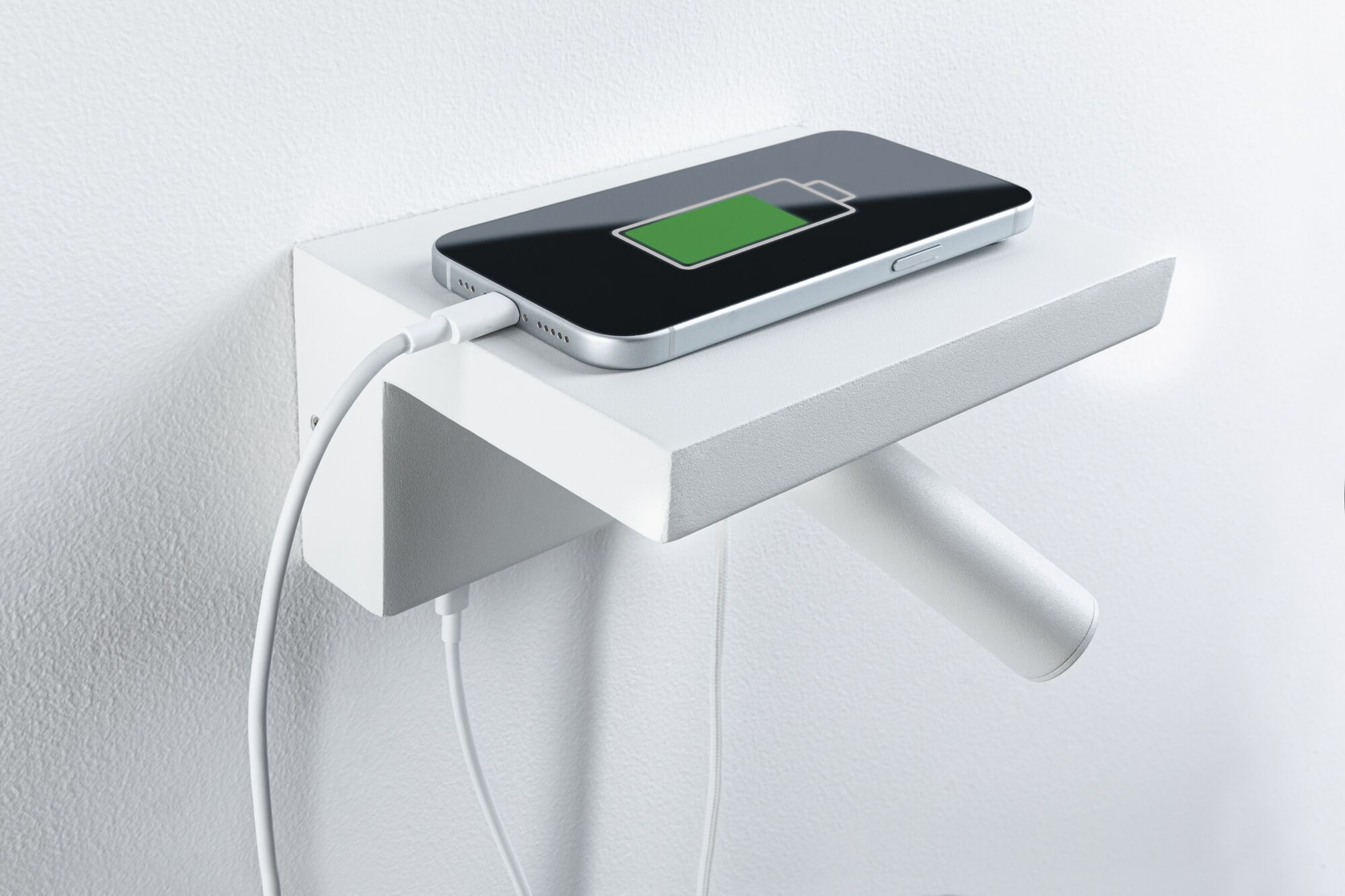 Ein Smartphone lädt auf einem kleinen, weißen Regal an einer Wand.