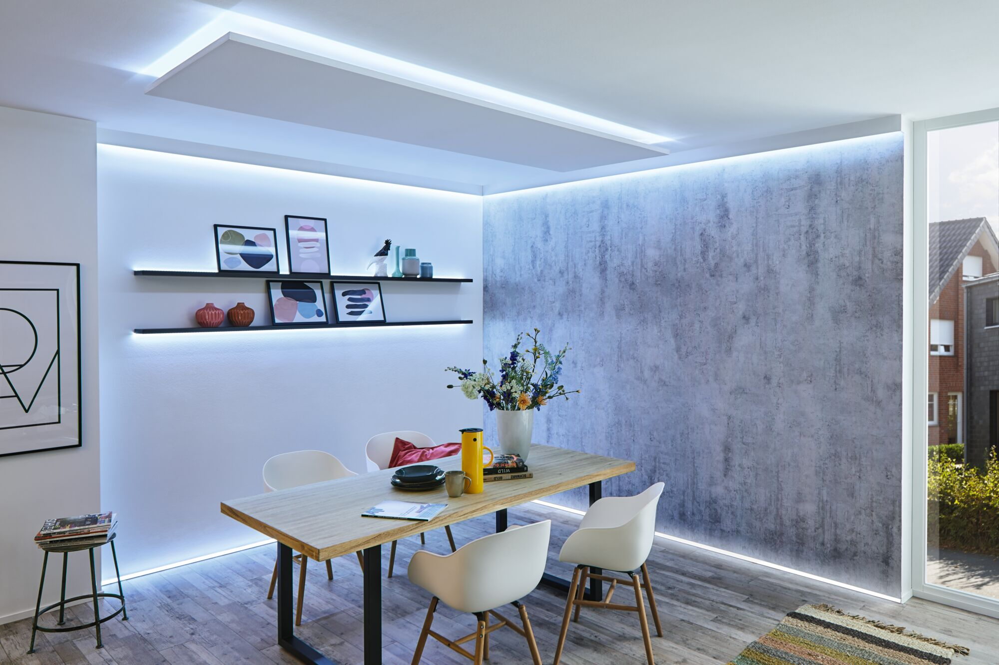 Moderne Esszimmer mit Holztisch, weißen Stühlen, beleuchteten Wänden und Wandregalen mit Bildern.