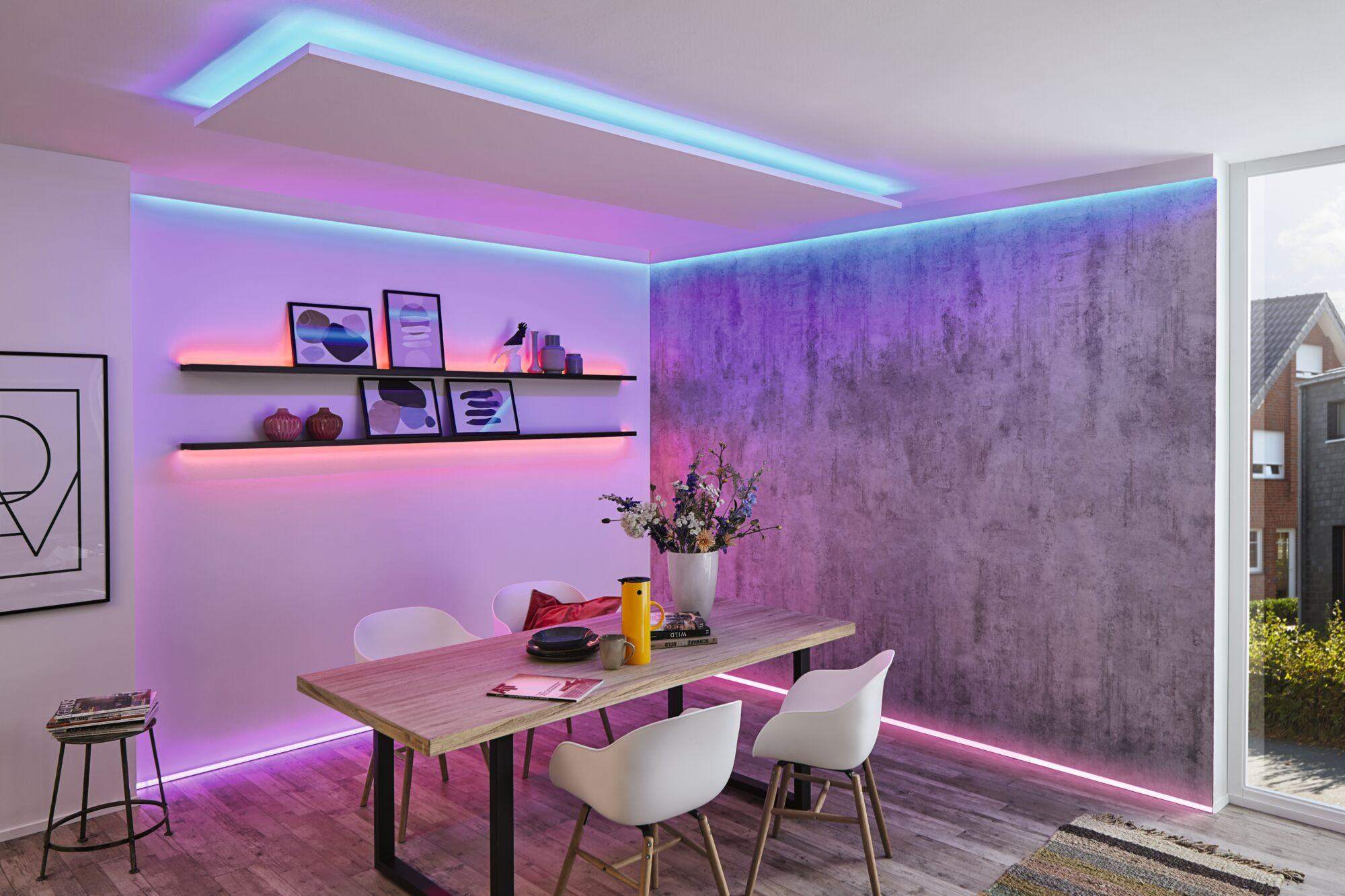 Ein modernes Esszimmer mit Holztisch, weißen Stühlen, Regalen und lebendiger lila und blauer Raumbeleuchtung.