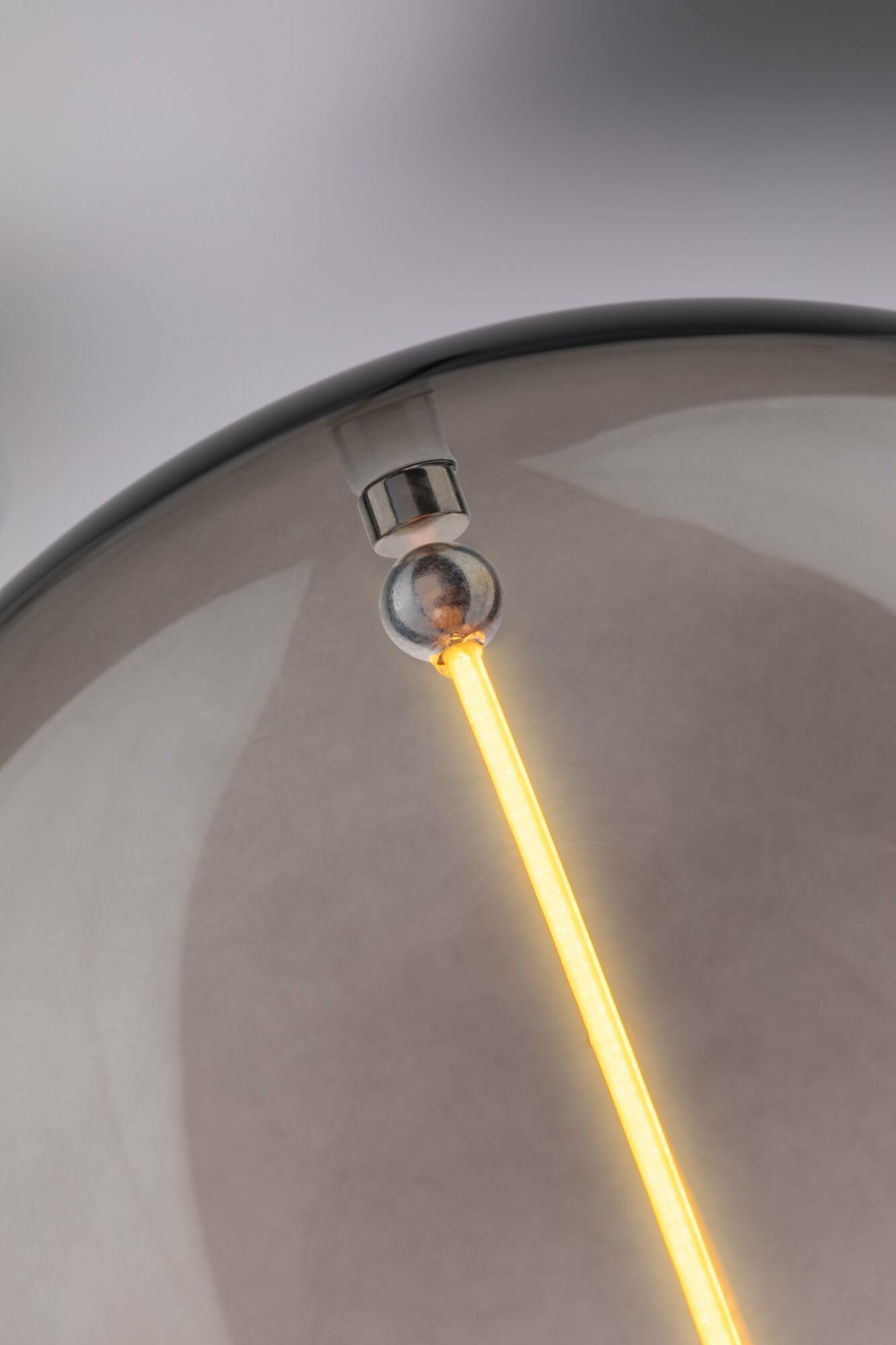 Nahaufnahme eines leuchtenden gelben LED-Filaments in einer getönten Glaskugellampe mit Silberverbinder.