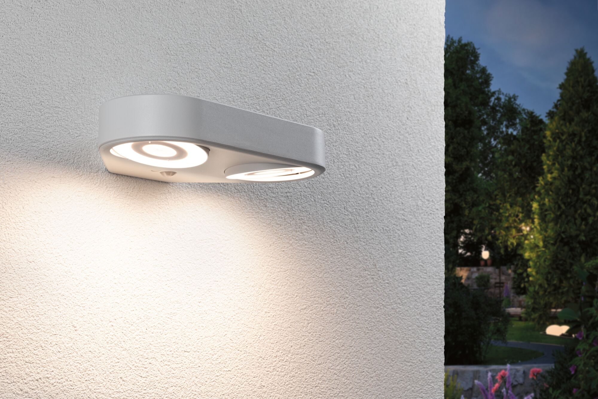 Nowoczesna, biała, owalna lampa ścienna zewnętrzna z dwiema świecącymi soczewkami LED zamontowana na ścianie o zmierzchu.