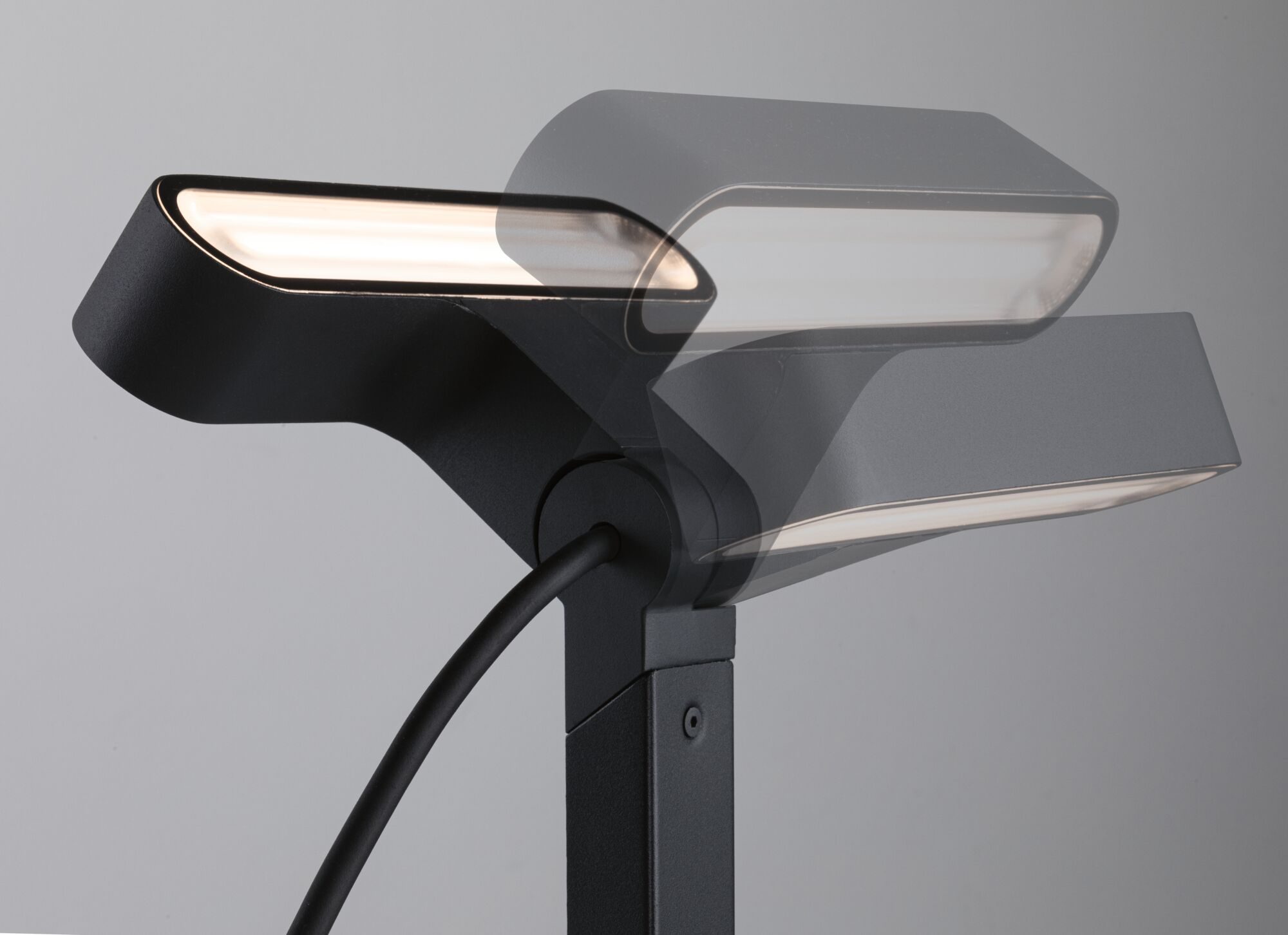 Eine verstellbare schwarze Schreibtischlampe leuchtet auf einem grauen Hintergrund, demonstriert durch Bewegung.