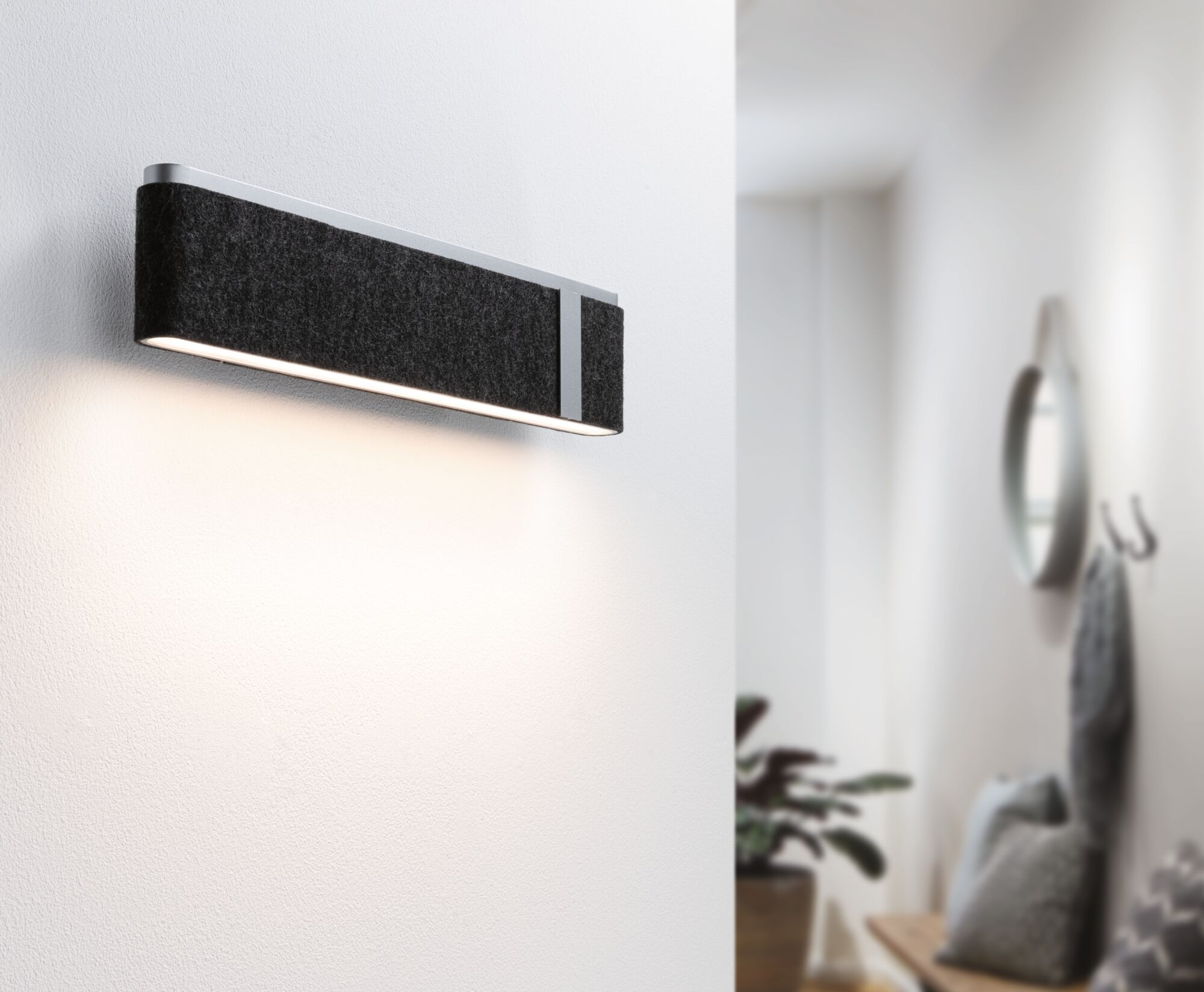 Eine schwarze Filzwandleuchte ist an einer weißen Wand montiert und wirft in einem modernen Flur Licht nach unten.