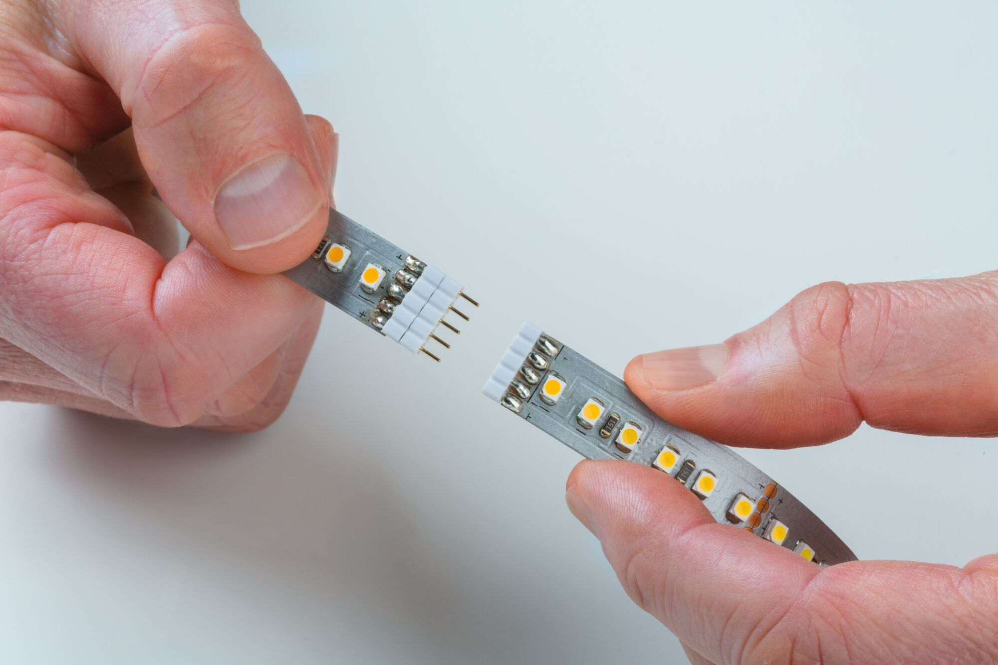 Hände halten zwei LED-Streifen, die mit Stiften verbunden werden sollen.