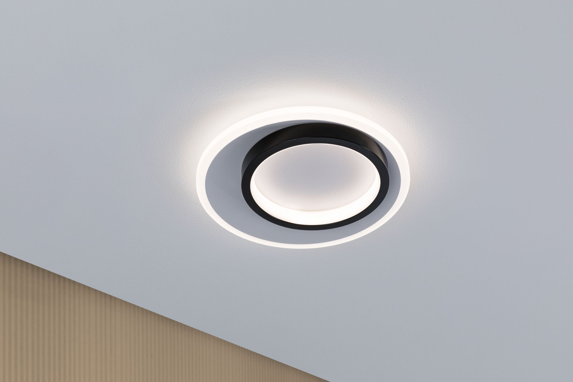 Eine moderne schwarz-weiße Deckenleuchte an einer weißen Decke mit einer strukturierten Wand in der Ecke.