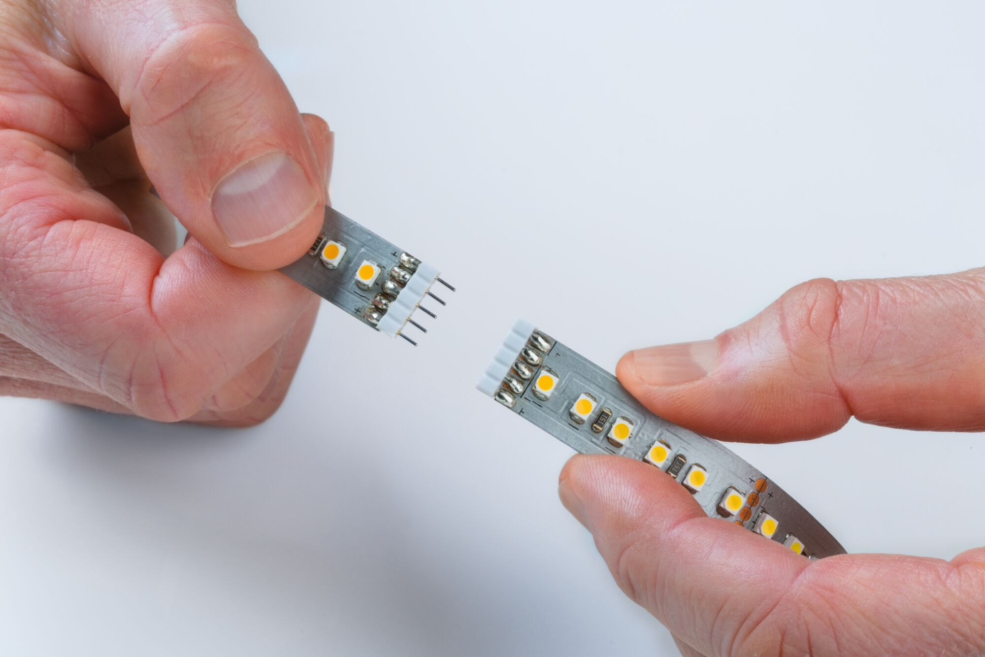 Hände halten zwei LED-Streifen mit Pins auf weißem Hintergrund.