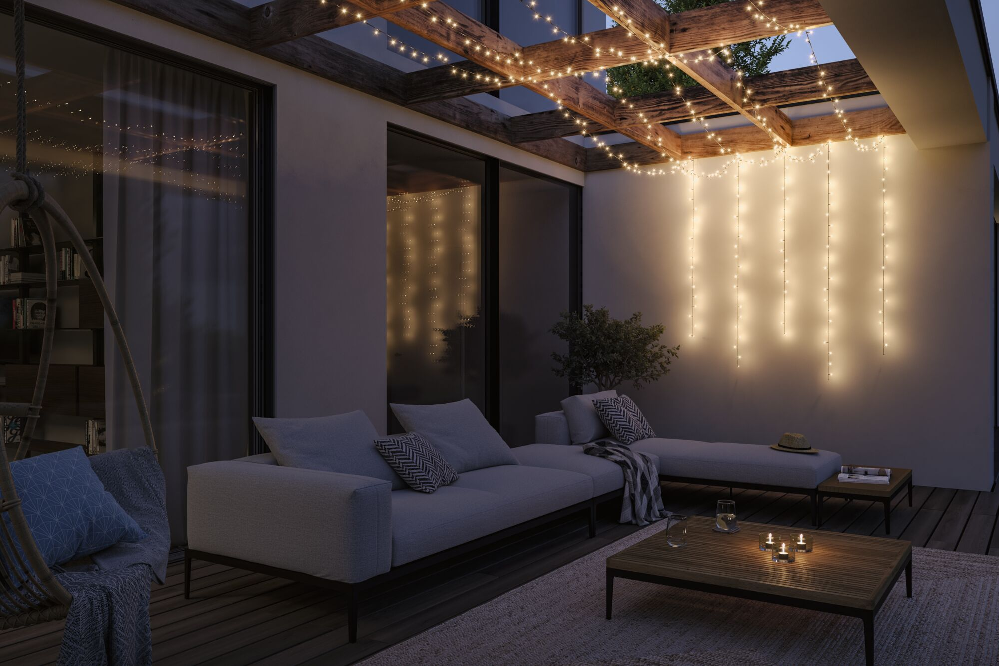 Eine gemütliche, abendliche Terrasse mit Lichterketten, modernen Sofas und Holztischen.