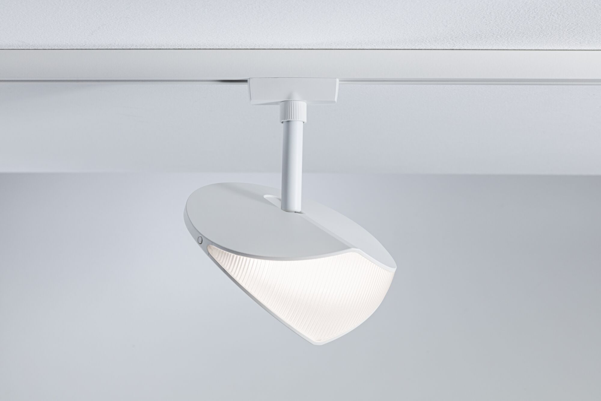 Eine moderne weiße Schienenleuchte an der Decke mit einem beleuchteten, gerippten Schirm nach unten geneigt.