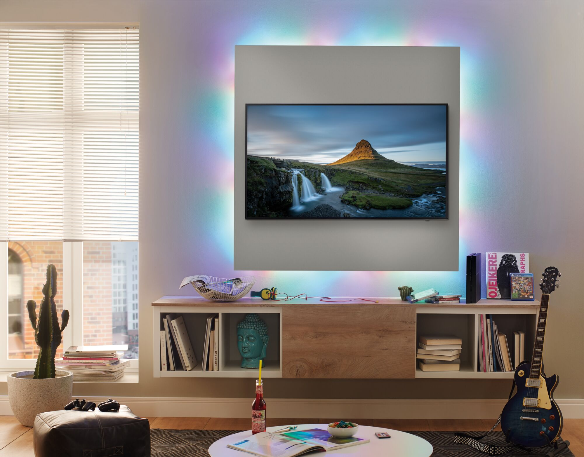 Wohnzimmer mit Fernseher und bunter Hintergrundbeleuchtung, Regal, Gitarre und Pflanzen.