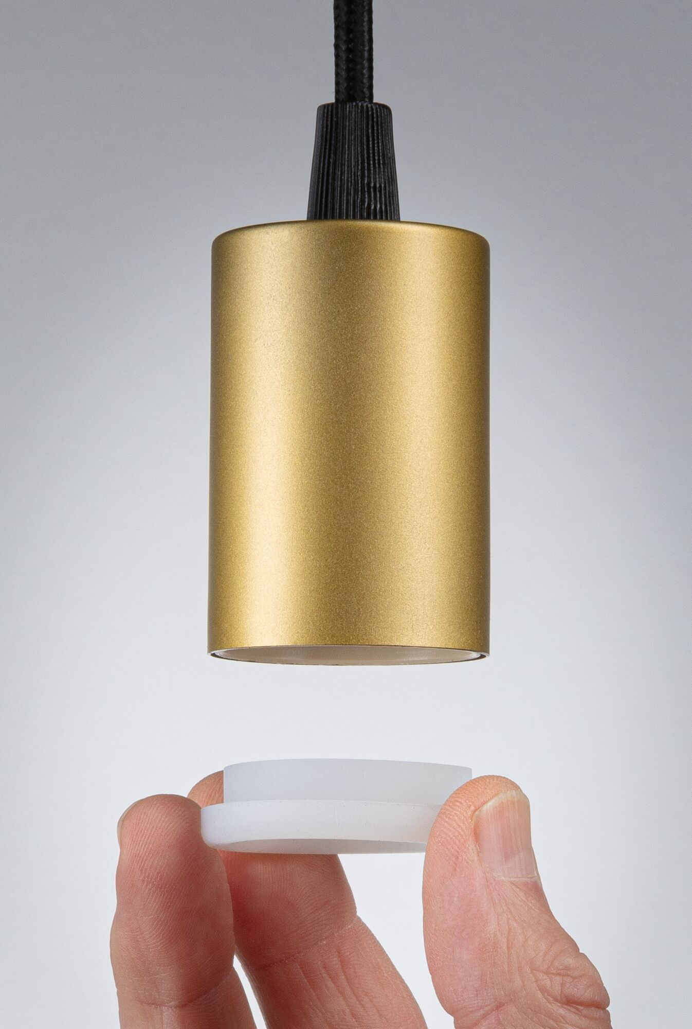 Eine Hand hält einen weißen Ring unter eine goldene Lampenfassung.