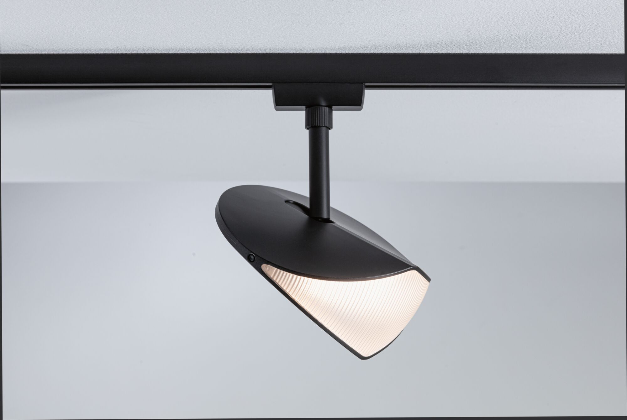 Eine schwarze Schienenleuchte mit geripptem, leuchtendem Diffusor hängt an einer Decke.