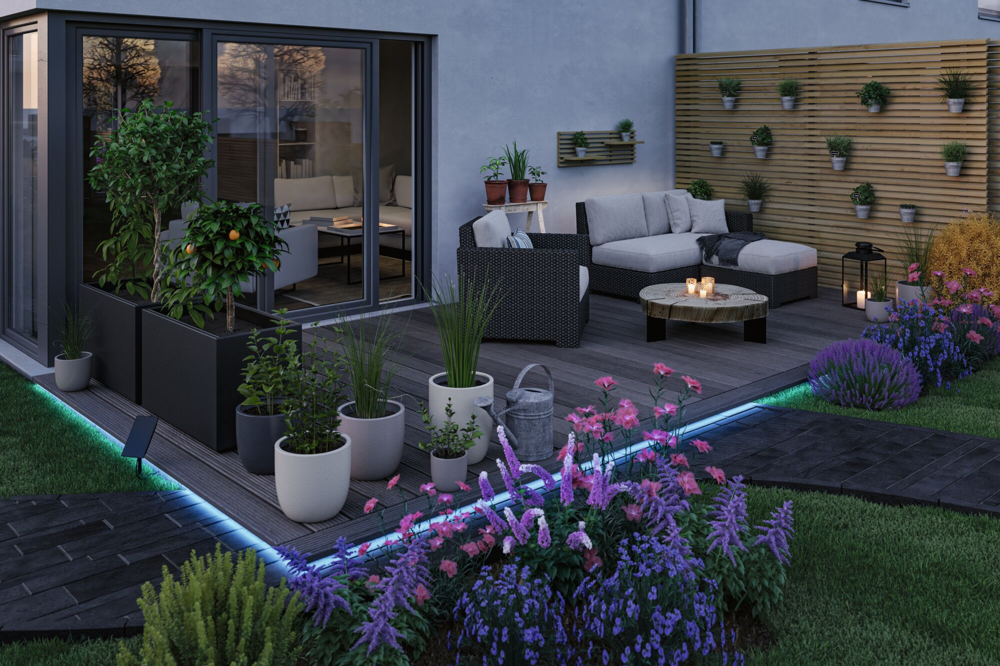 Moderne Holzterrasse mit gemütlichen Möbeln, vielen Topfpflanzen und beleuchteten Blumenbeeten bei Dämmerung.